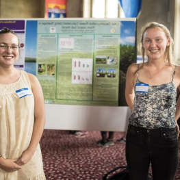 Two students smiling in front of a research poster in the Great Hall